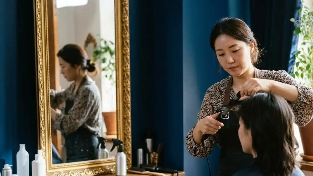 A hair stylist styling a customer's hair in front of a gold-framed mirror