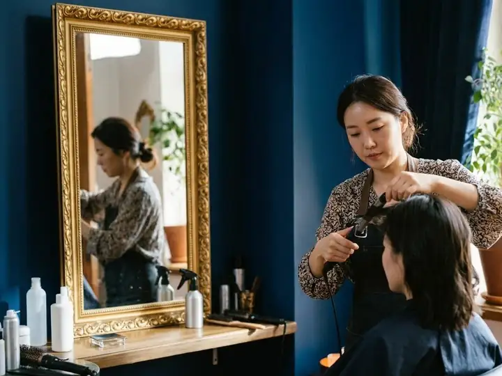 A hair stylist styling a customer's hair in front of a gold-framed mirror