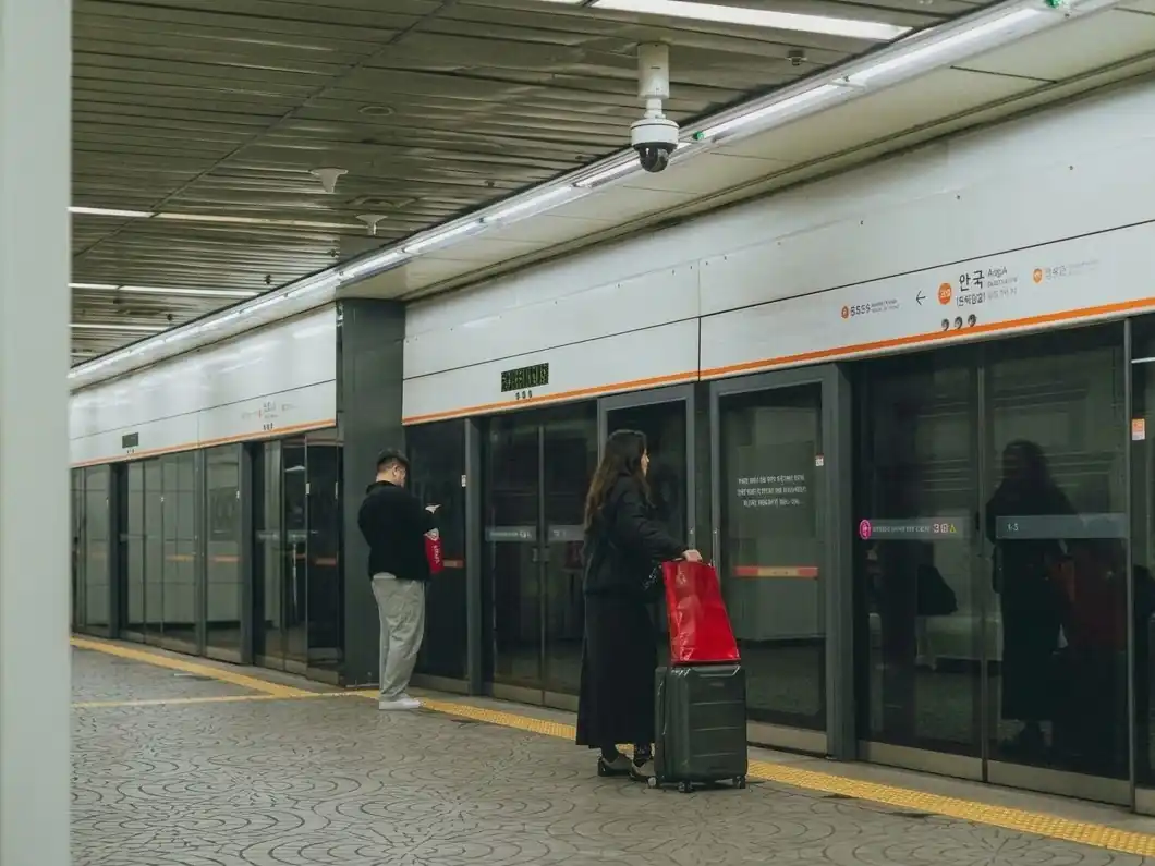 A Seoul subway platform with travelers and a suitcase
