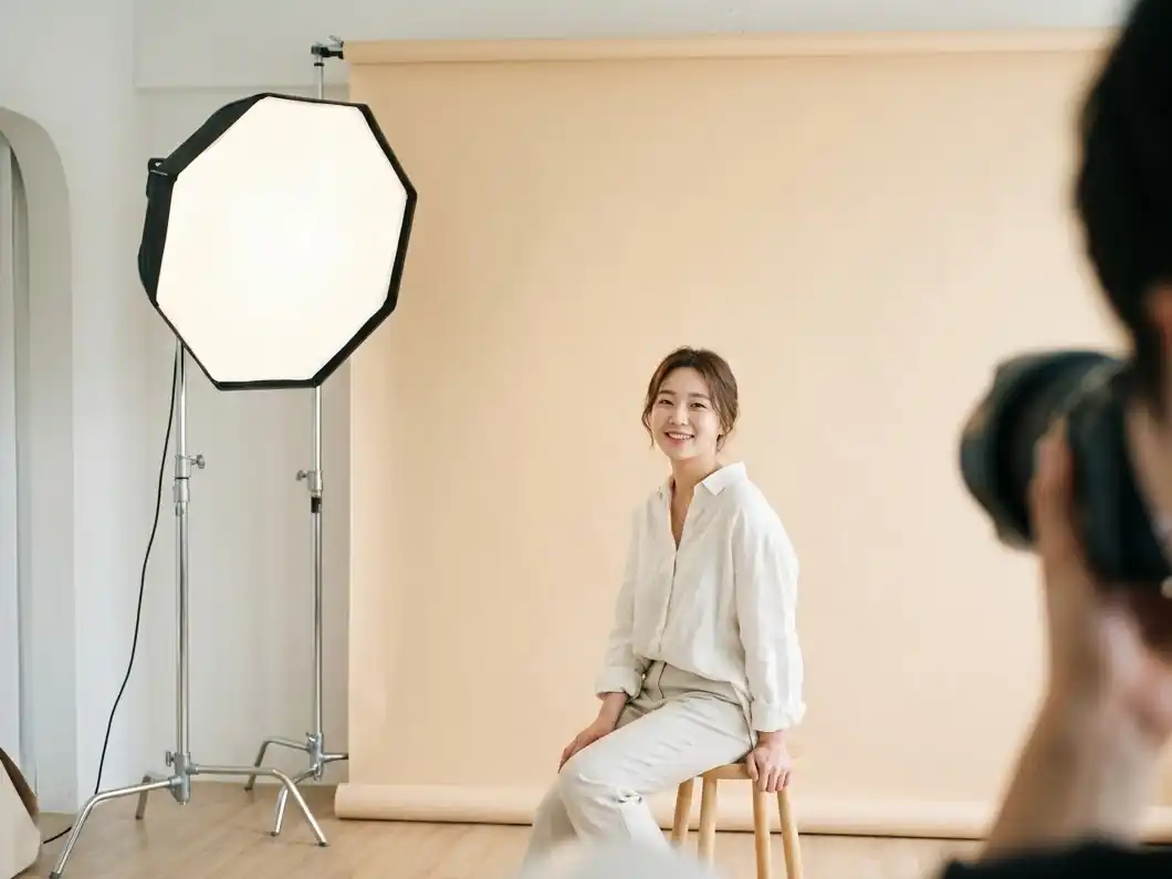 A photographer shooting a smiling woman on a stool in a bright studio